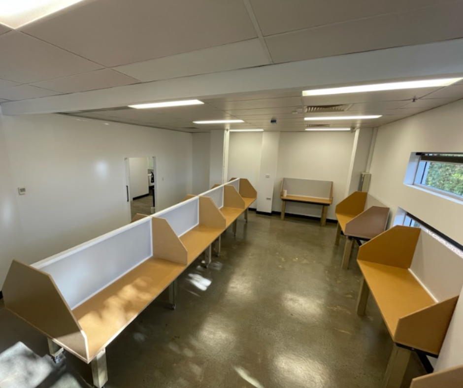 Empty office with rows of tan study pods, white walls, and overhead fluorescent lights