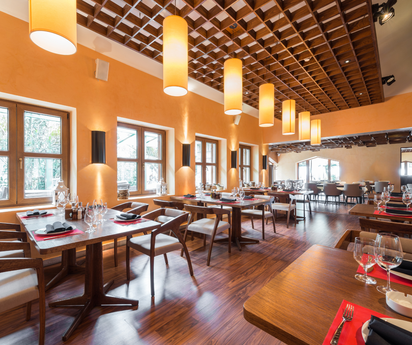 Bright restaurant dining room with wooden tables, hanging pendant lights, and large windows over hardwood floors