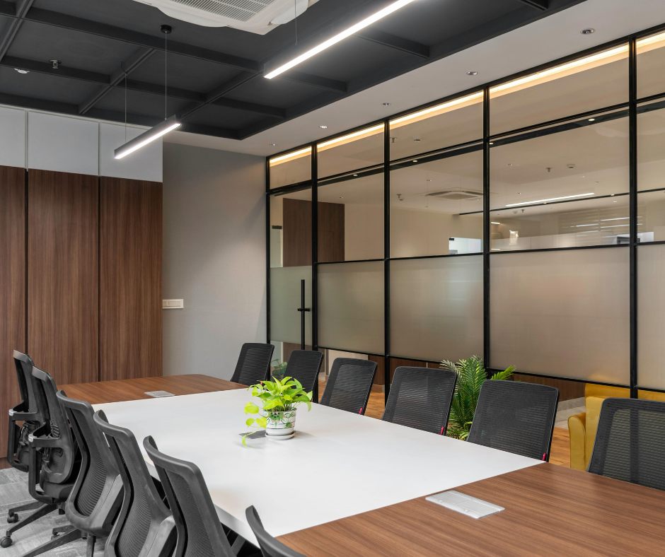 Modern conference room with a white table, black chairs, wood accents, and glass partition walls