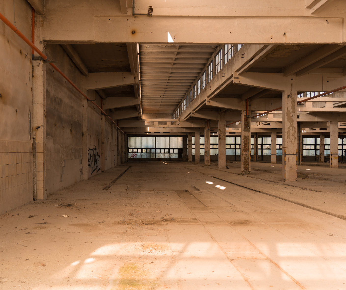 Empty unfinished warehouse interior with concrete columns, dusty floor, and overhead beams Empty unfinished warehouse interior with concrete columns, dusty floor, and overhead beams