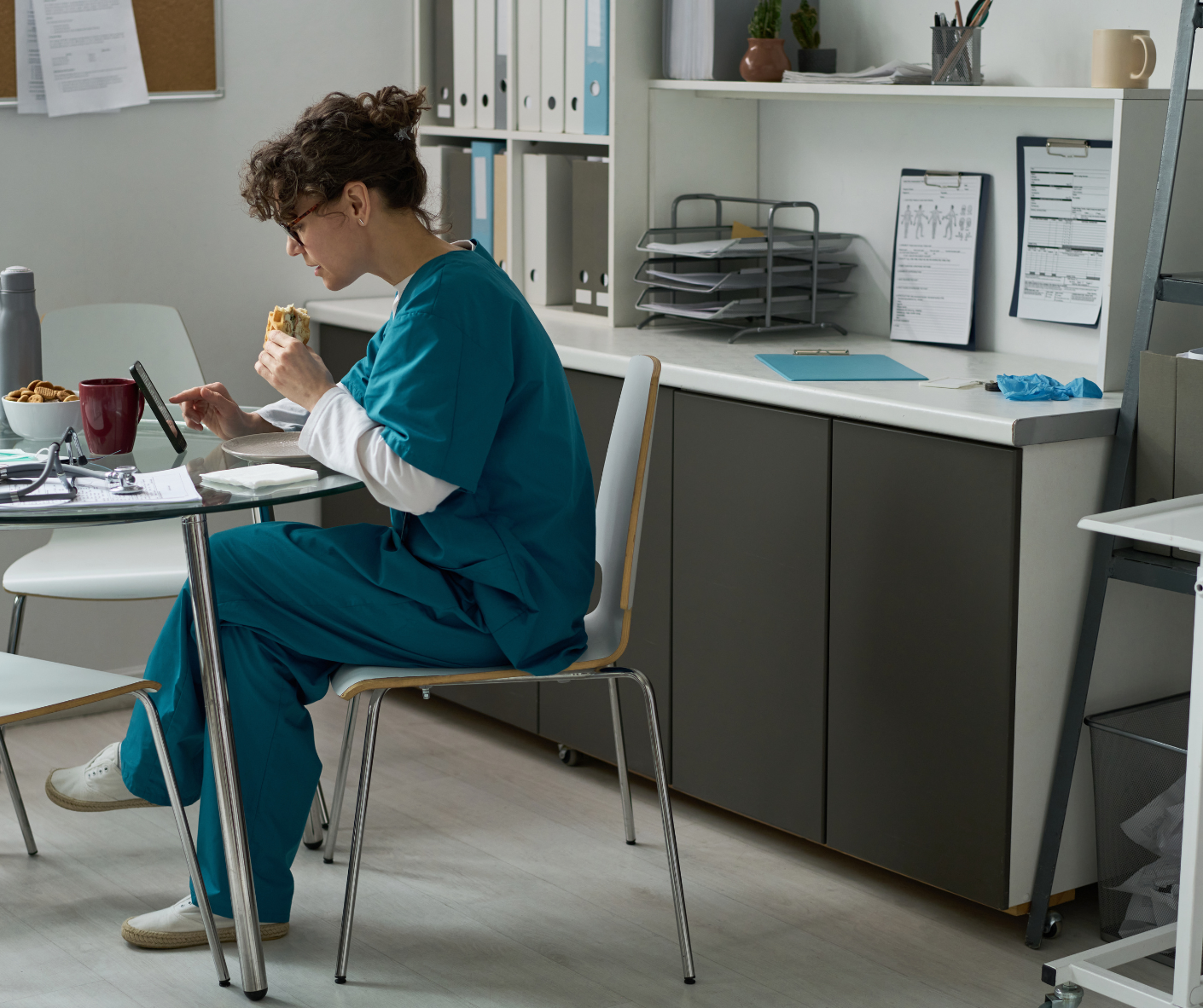 Person in teal scrubs eating at a desk in a clinic office. Person in teal scrubs eating at a desk in a clinic office.