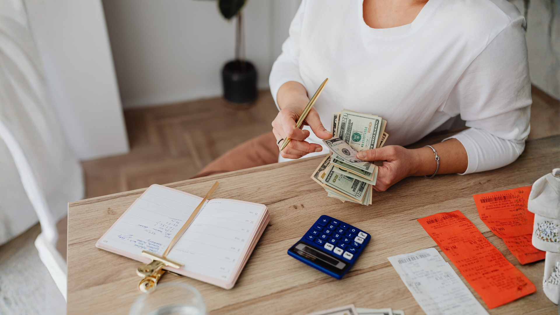 Person counting U.S. dollar bills while reviewing receipts with a calculator and planner on a table. Person counting U.S. dollar bills while reviewing receipts with a calculator and planner on a table.