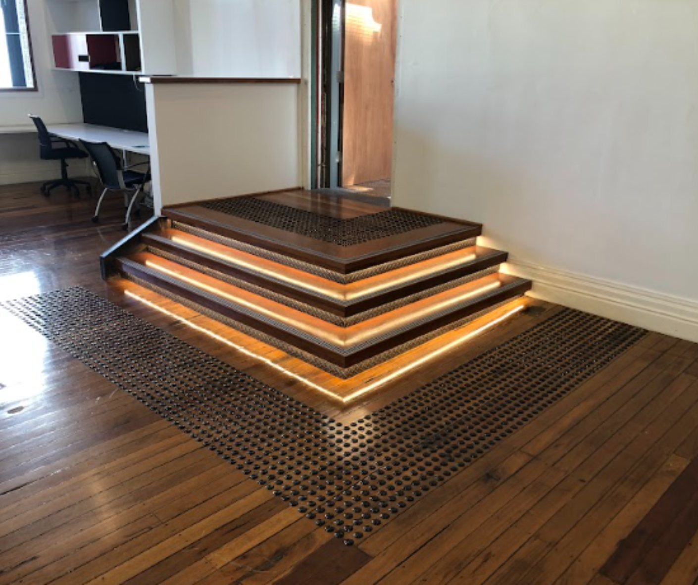 Illuminated tiered wooden platform with handrail on a woven rug in an office space Illuminated tiered wooden platform with handrail on a woven rug in an office space