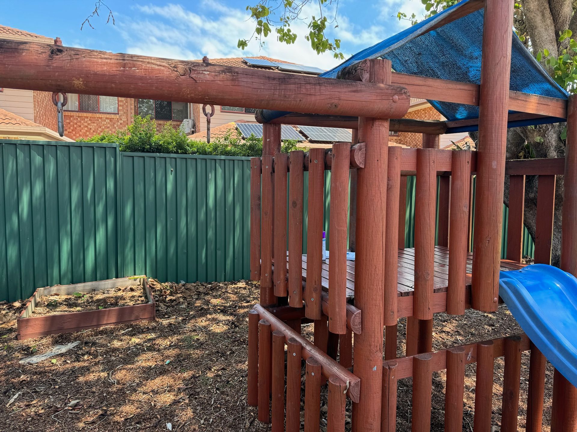 A wooden playground with a slide and a fence in the background.