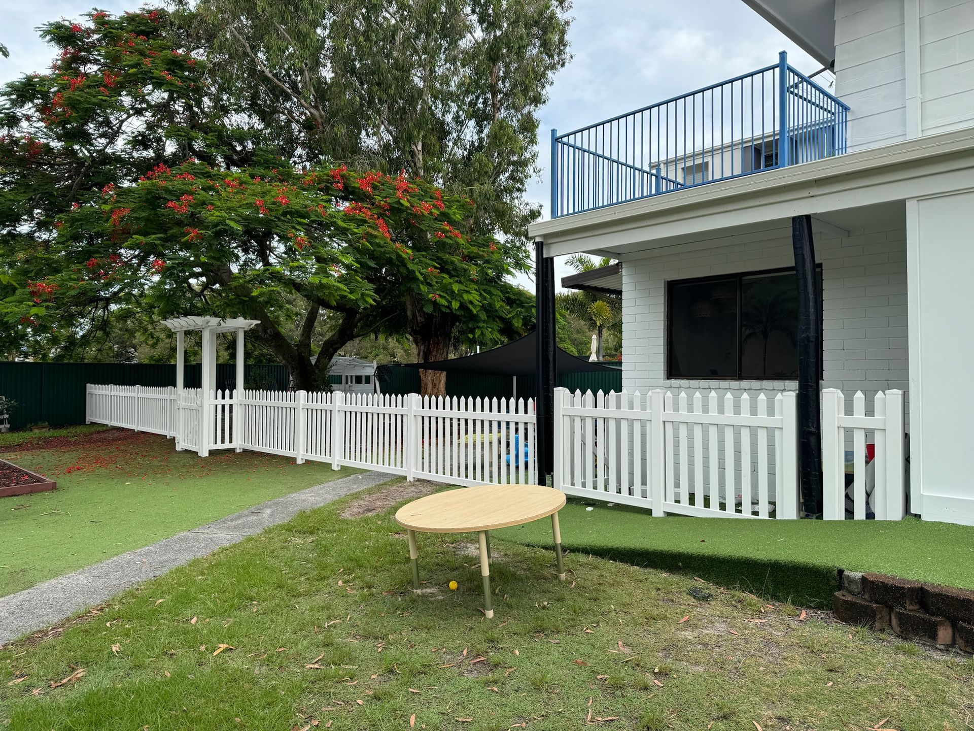 A white picket fence surrounds a house with a table in front of it.