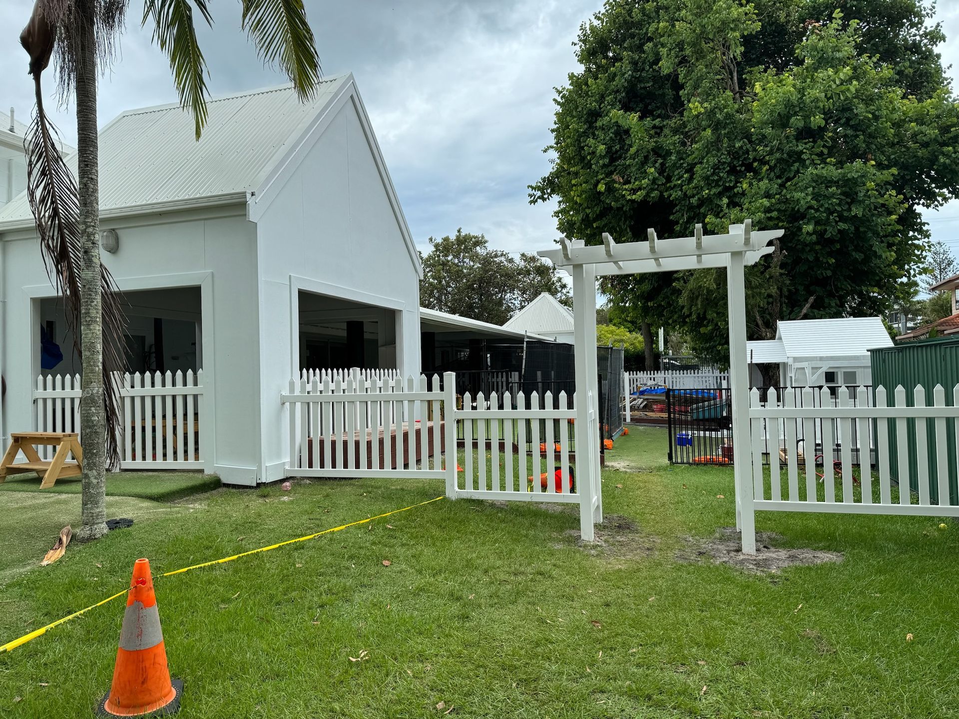 A white house with a white picket fence and a pergola in front of it.