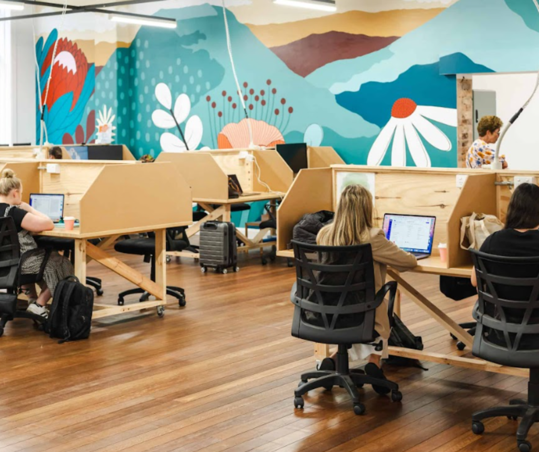 People working at computers in a colorful open-plan office with wood floors and privacy desk dividers People working at computers in a colorful open-plan office with wood floors and privacy desk dividers