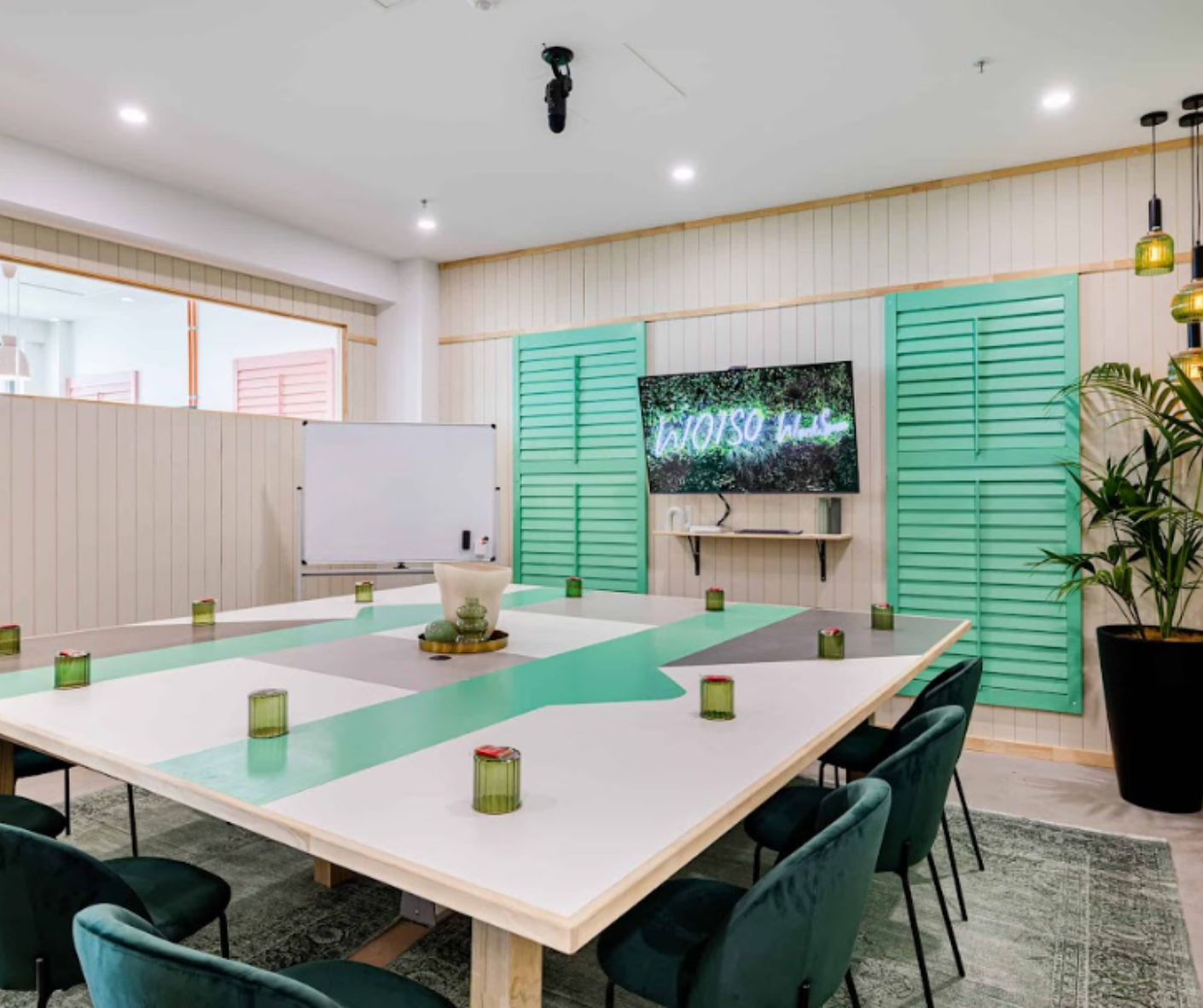 Bright meeting room with long tables, green chairs, whiteboard, and green shutters on the wall Bright meeting room with long tables, green chairs, whiteboard, and green shutters on the wall