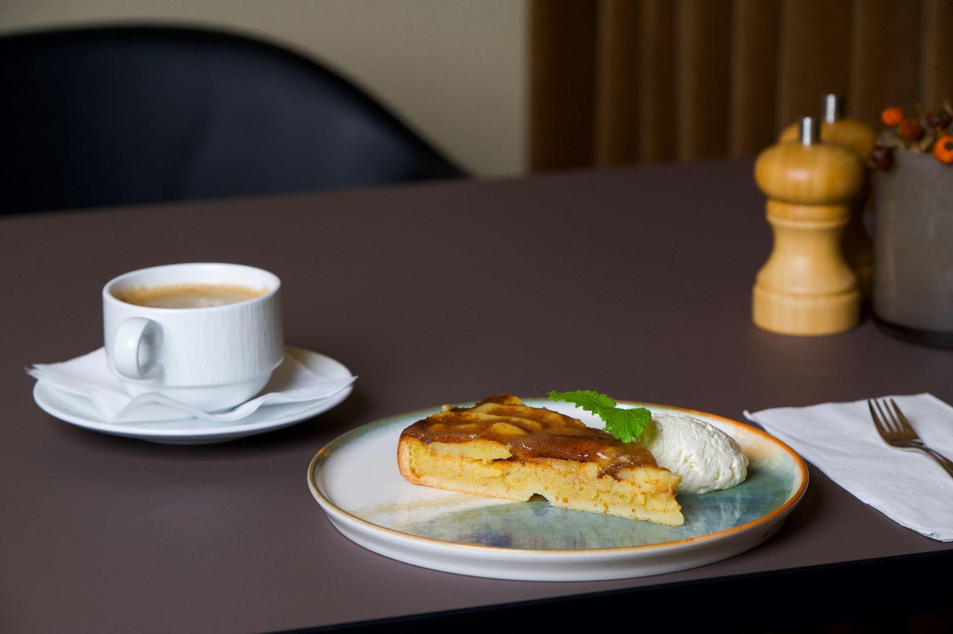 Kaffe, æblekage med fløde og en gaffel på et bord.