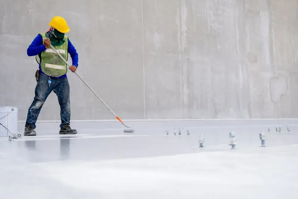 A Construction Worker Is Painting a Concrete Floor with A Roller — Concrete Colour Solutions in Port Stephens, NSW