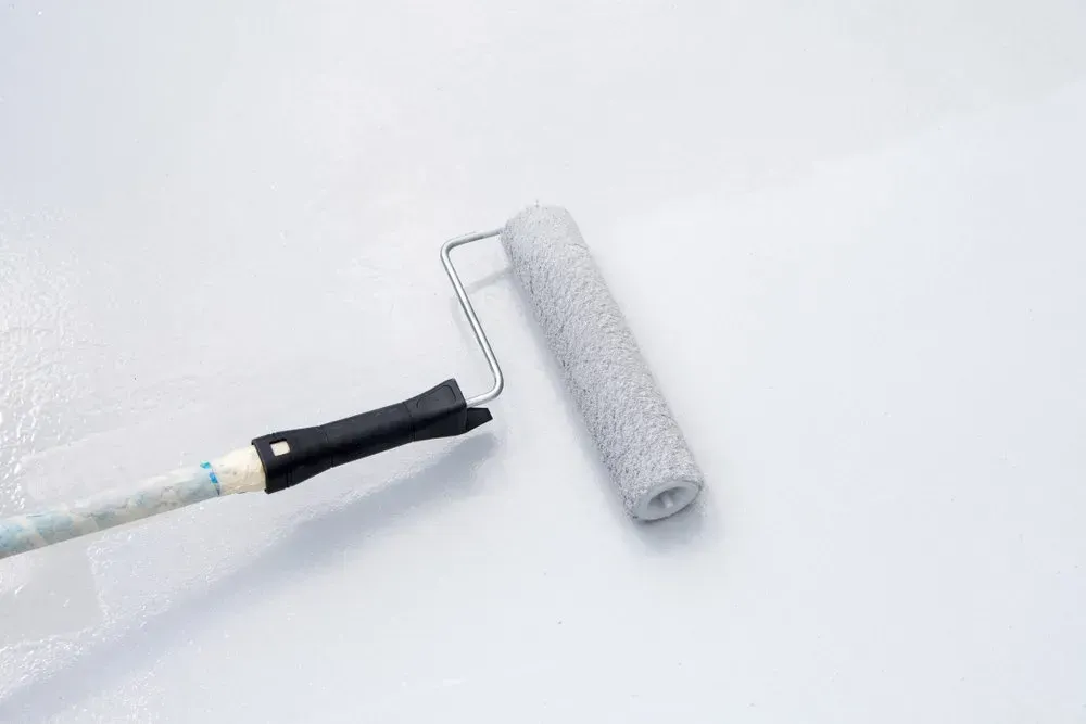 A Paint Roller Is Being Used to Paint a White Wall — Concrete Colour Solutions in Lake Macquarie, NSW