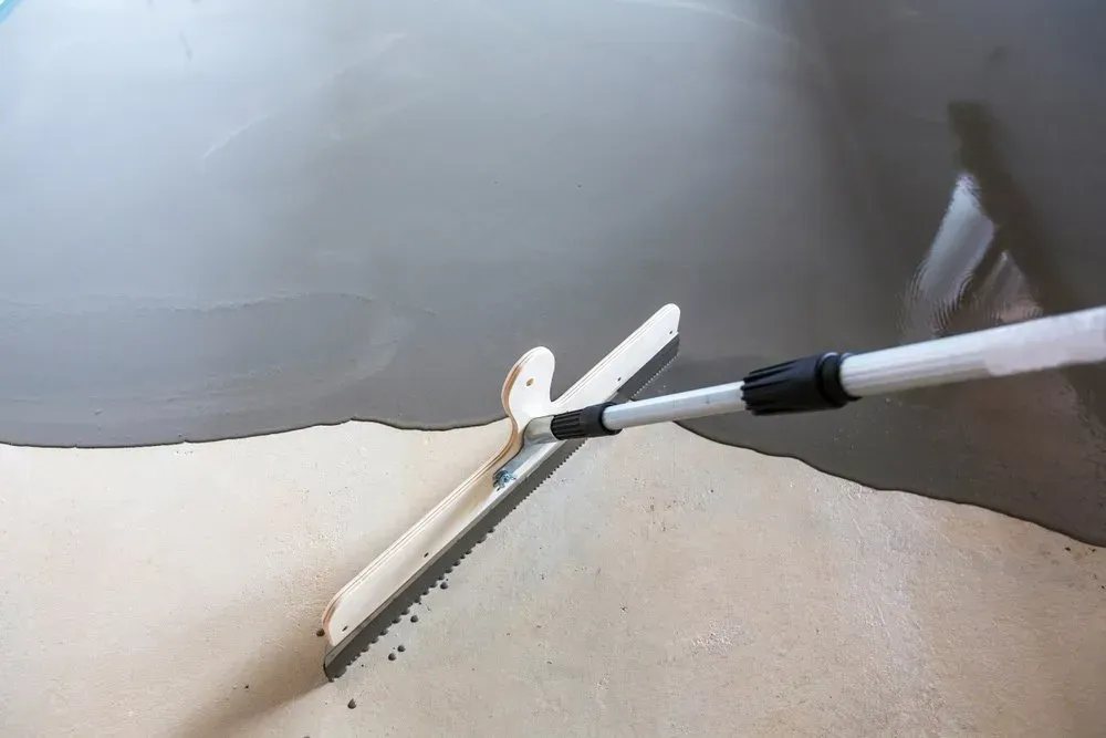 A Person Is Spreading Concrete on The Floor with A Trowel — Concrete Colour Solutions in Heatherbrae, NSW