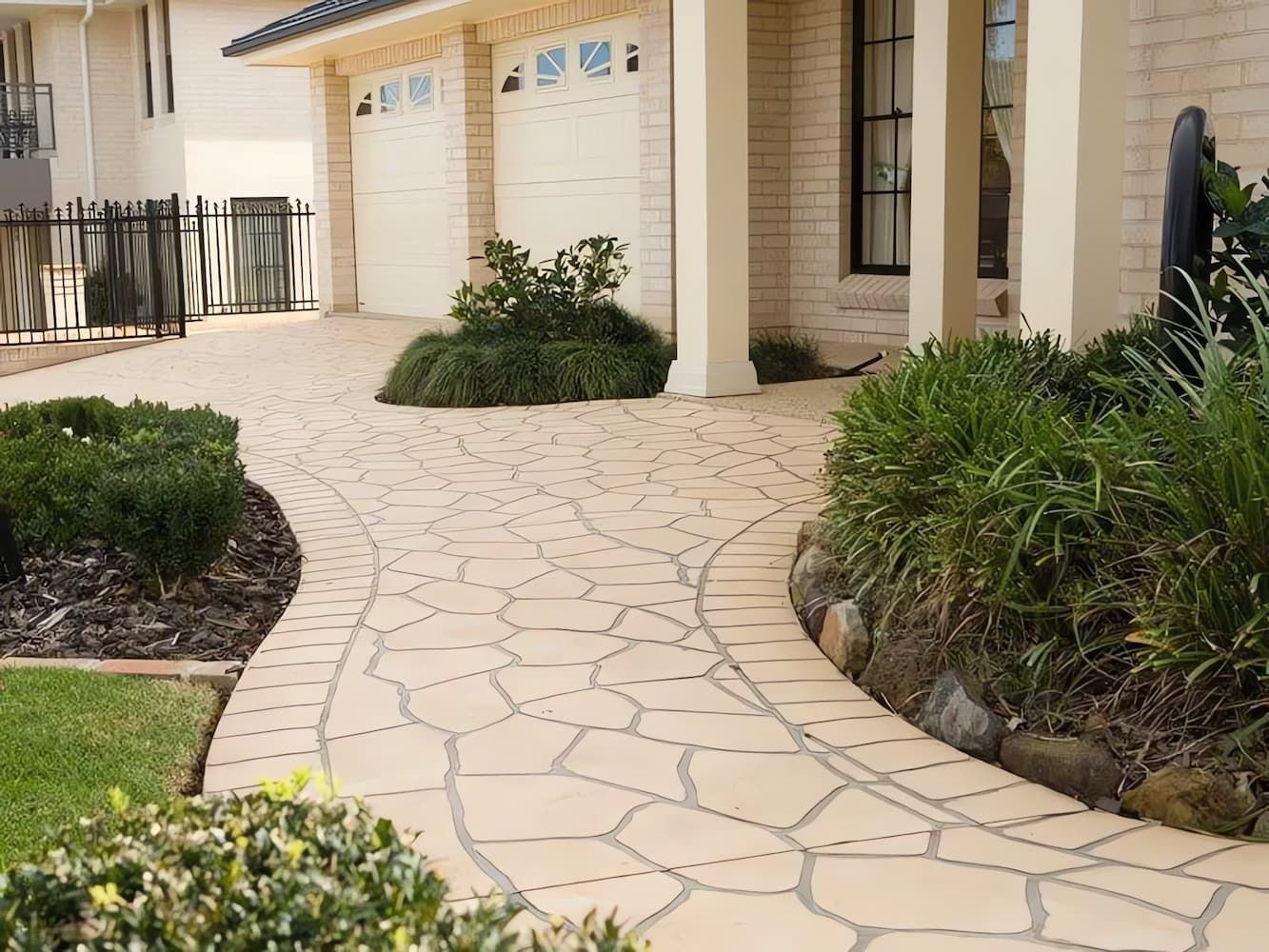 Curved Stone Walkway Leading to a House Entrance, Bordered by Green Shrubs — Concrete Colour Solutions in Singleton, NSW