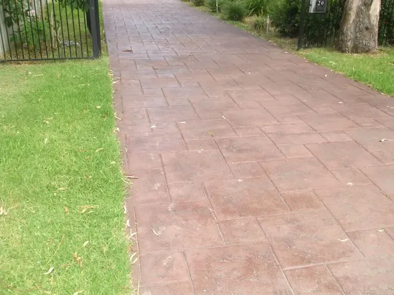 A brick driveway leading to a gate surrounded by grass.— Concrete Colour Solutions in Morisset, NSW