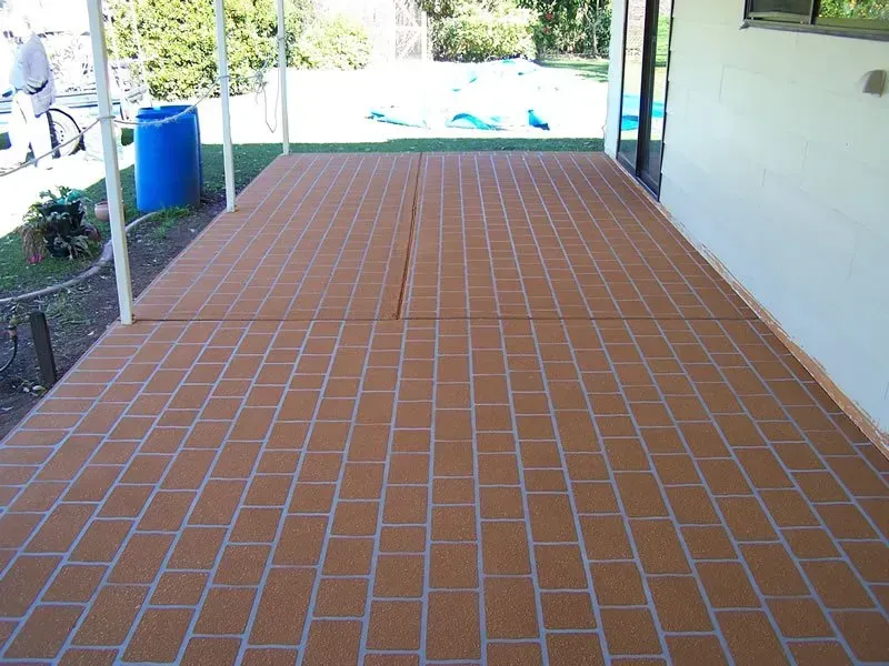 Covered Brick Patio With a Brown Tiled Floor and Blue Barrel Beside a House — Concrete Colour Solutions in Dungog, NSW