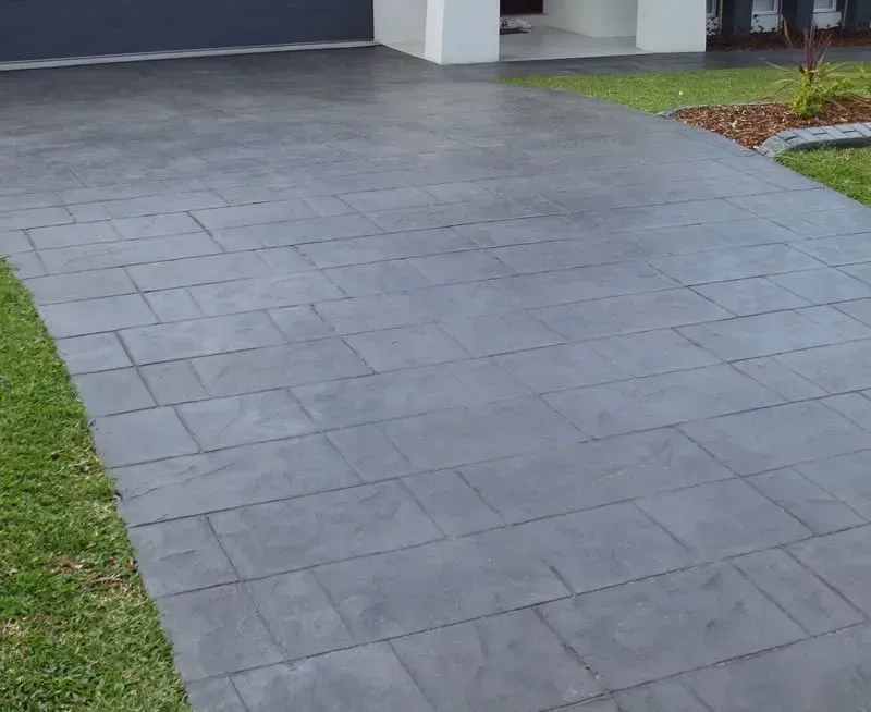 A concrete driveway leading to a house with grass on the side. — Concrete Colour Solutions in Morisset, NSW