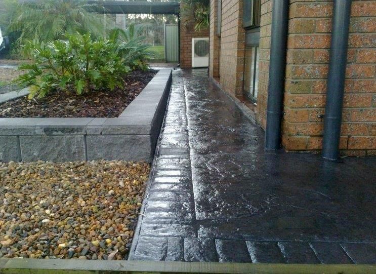 A brick building with a concrete walkway in front of it — Concrete Colour Solutions in Morisset, NSW