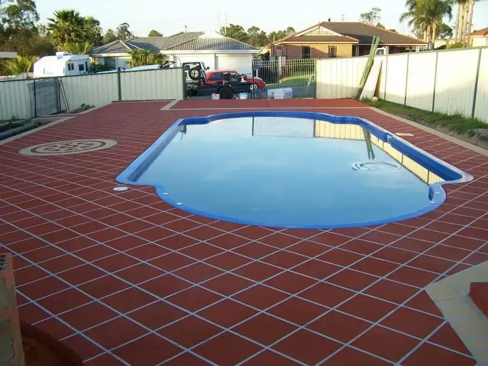 Backyard swimming pool covered by blue tarp, surrounded by red brick patio and white fence — Concrete Colour Solutions in Morisset, NSW