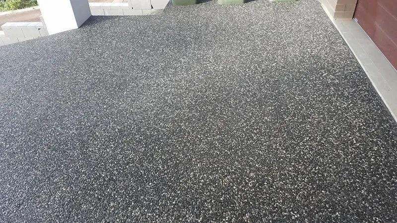 A close up of a black gravel floor next to a garage door. — Concrete Colour Solutions in Morisset, NSW