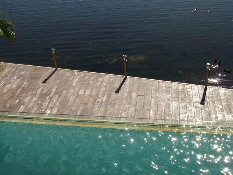 A swimming pool with a wooden deck next to a body of water — Concrete Colour Solutions in Morisset, NSW