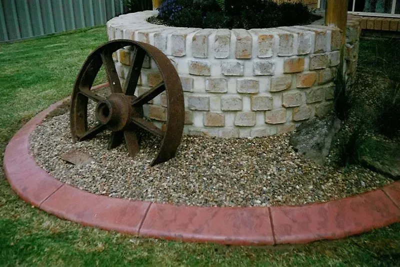 Old Wooden Wagon Wheel Beside a Stone Planter in a Landscaped Garded — Concrete Colour Solutions in Muswellbrook, NSW