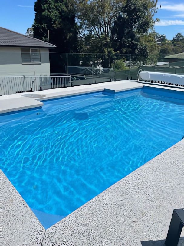 Bright Blue Backyard Swimming Pool Beside a House With White Coping — Concrete Colour Solutions in Scone, NSW