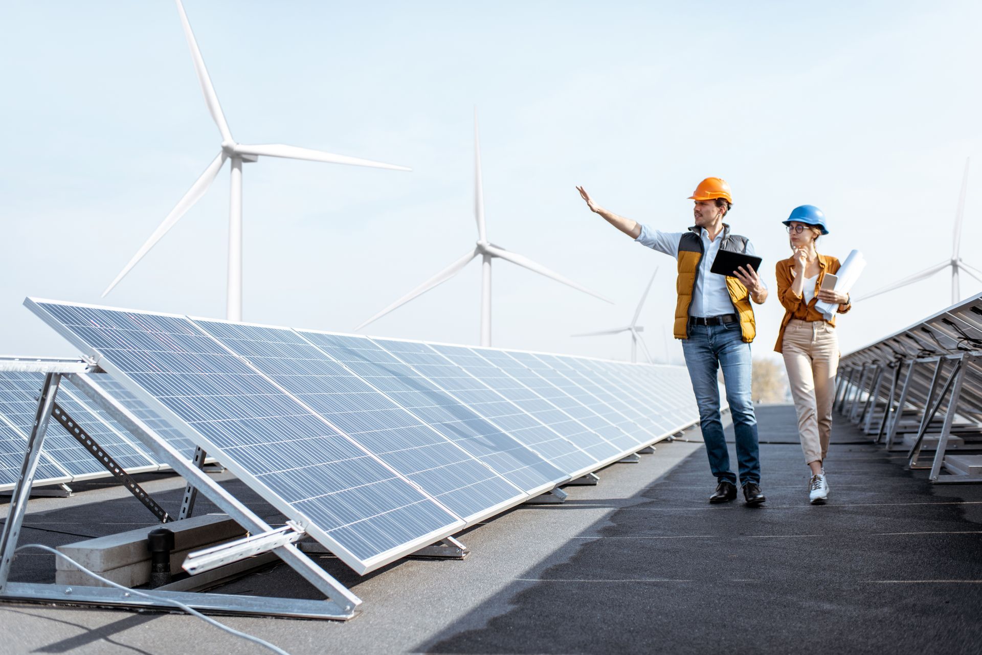 Engineers inspecting solar panels and wind turbines outdoors.