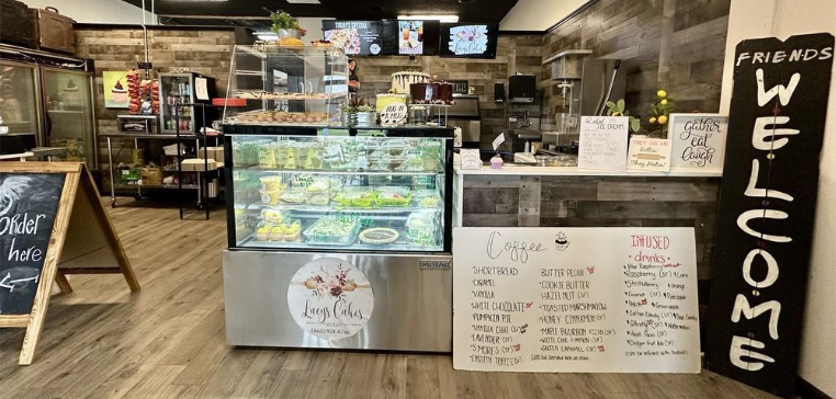 Interior of a cafe with a pastry display case, menu board, and a welcome sign.