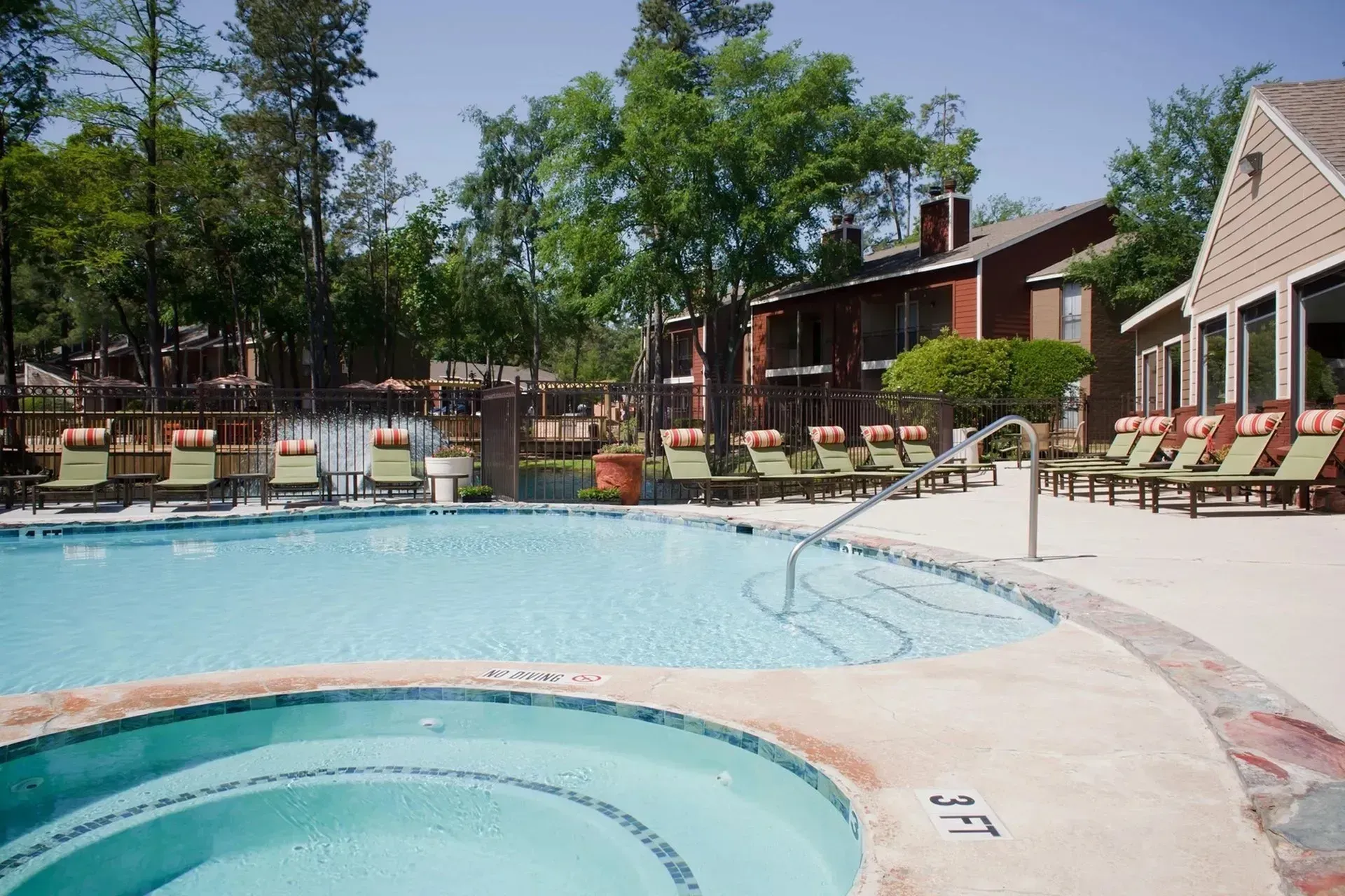 Swimming pool with lounge chairs, surrounded by trees and apartment buildings.