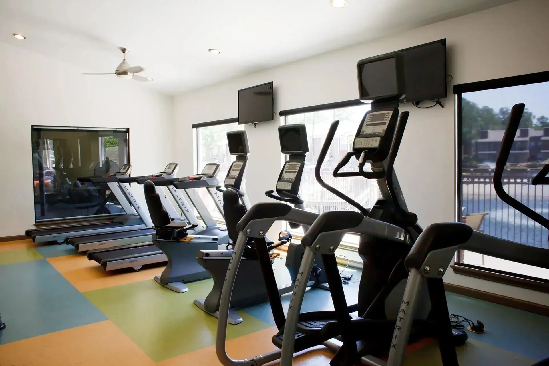Gym with treadmills, ellipticals, and stationary bikes, with televisions mounted on the wall.