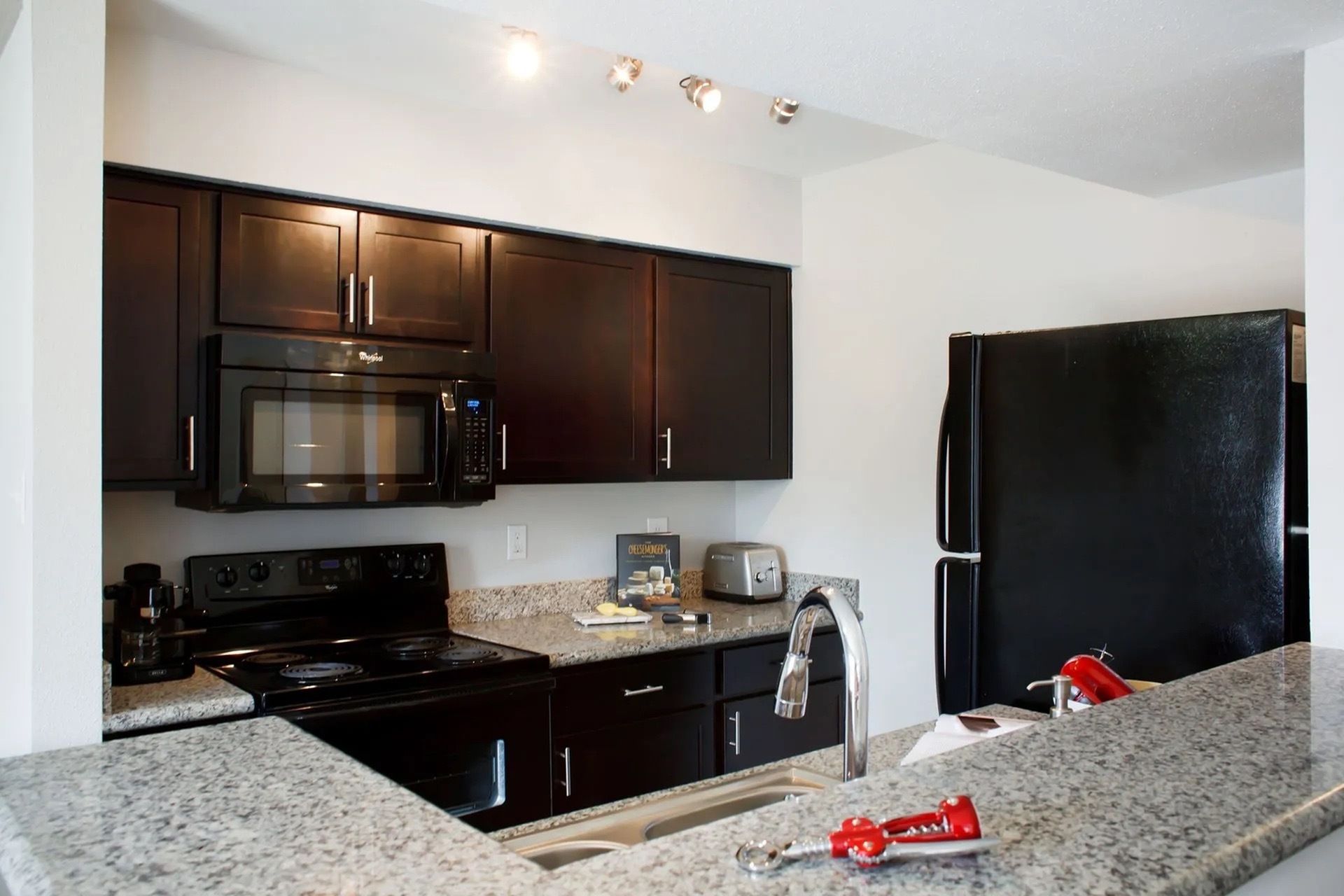 Apartment kitchen with dark wood cabinetry, granite counters, and stainless appliances.