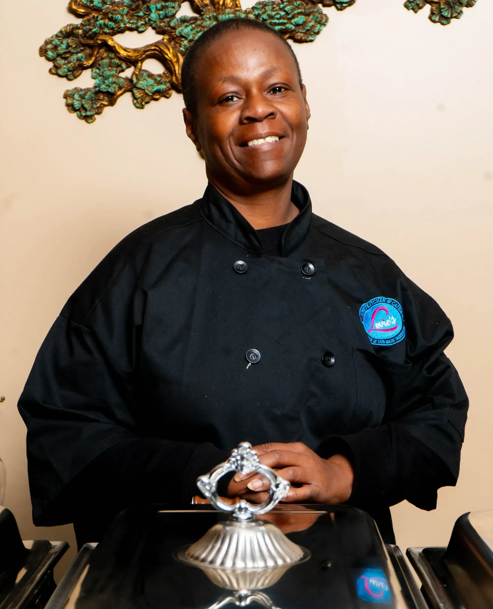 Chef in black uniform smiling behind a polished silver cloche display