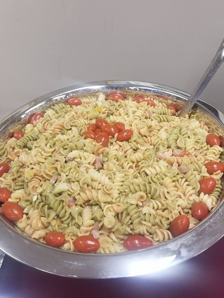 Large metal bowl of rotini pasta salad with cherry tomatoes and a serving spoon