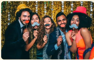 Five friends posing with novelty mustache props at a party in front of a gold sequin backdrop