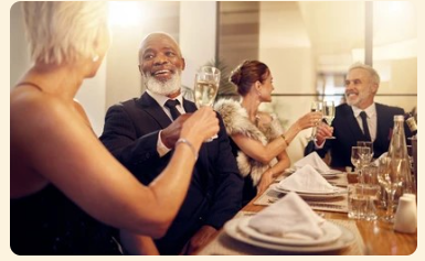 Guests toast at a warmly lit banquet table with wine glasses and folded napkins.