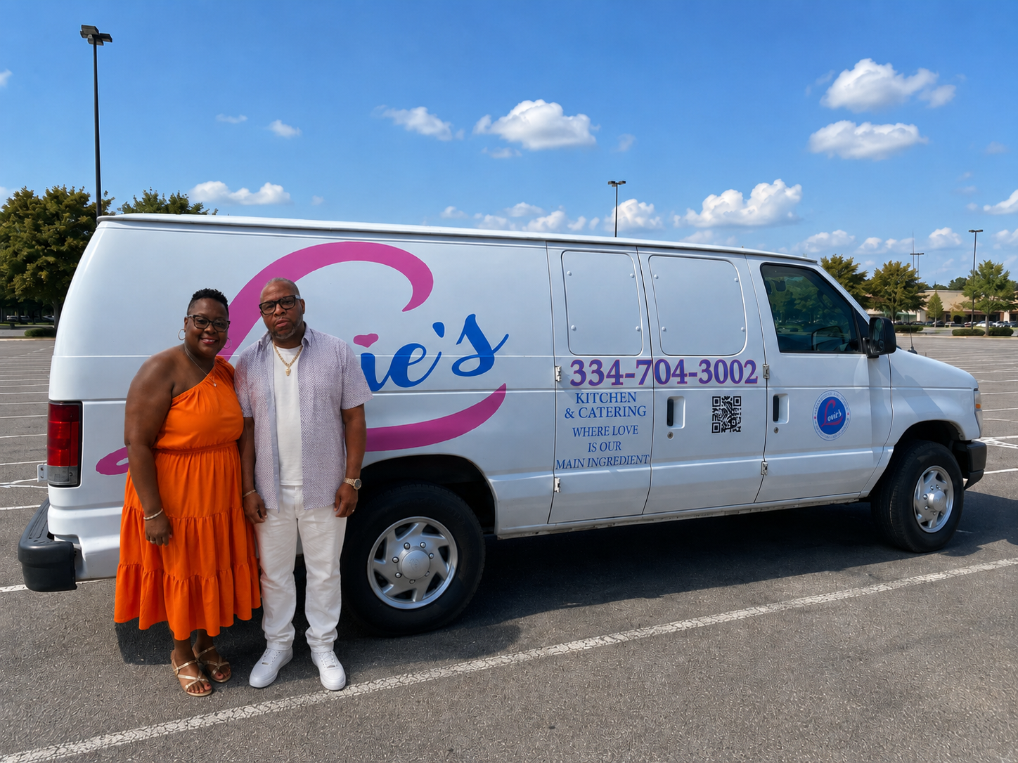 Two people standing beside a white van with pink logo and phone number in a parking lot under a blue sky