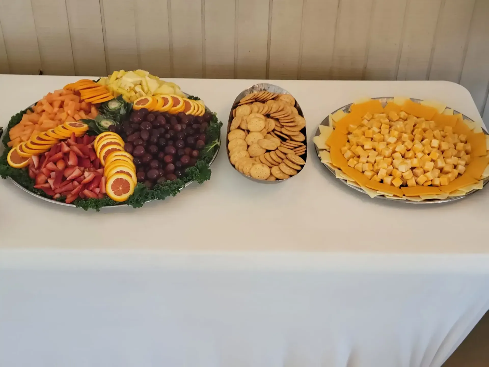 Table with three platters of assorted fruit and snacks, including grapes, pineapple, and crackers
