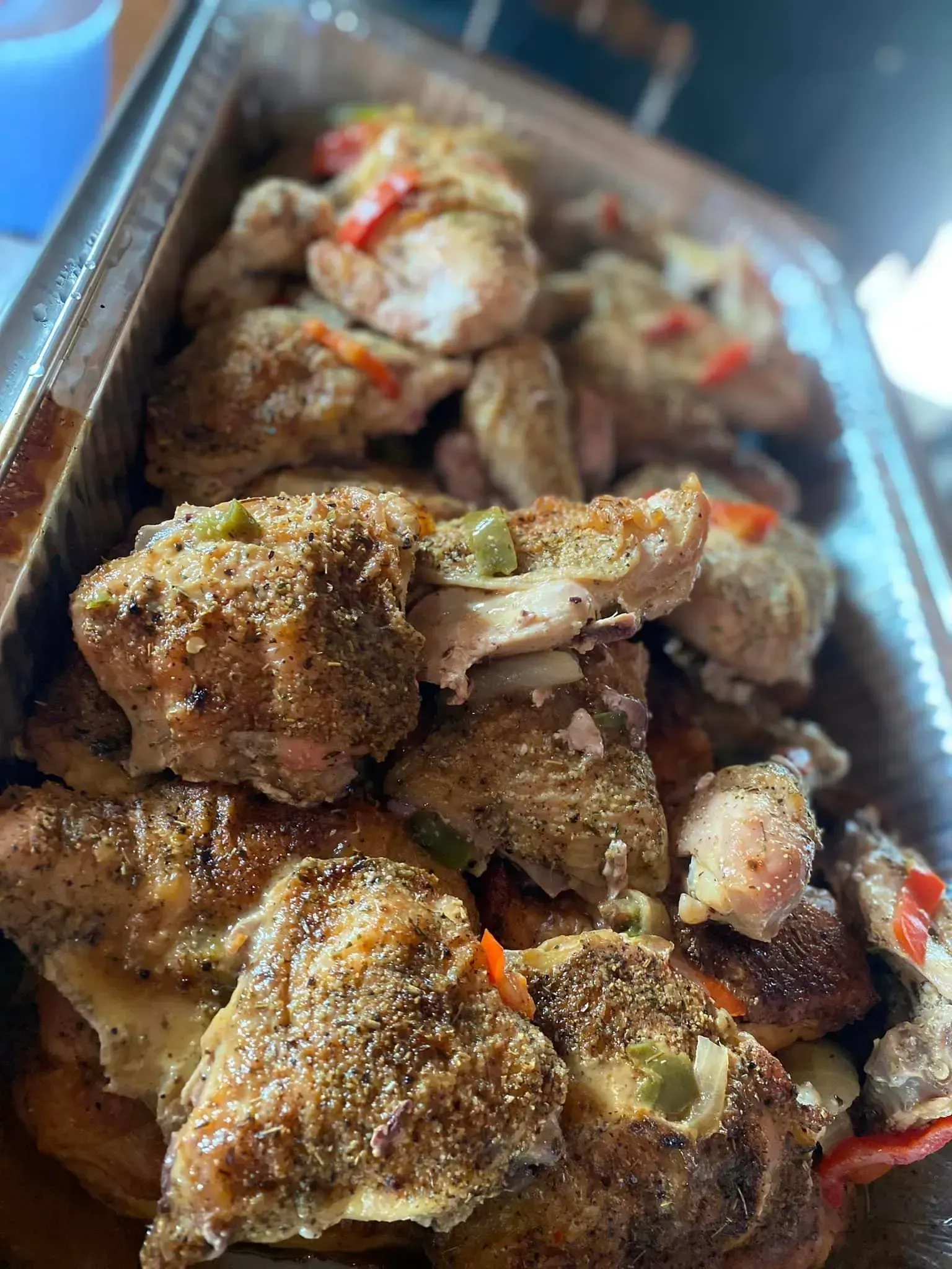 Tray of seasoned roasted chicken pieces with sauce and red pepper slices