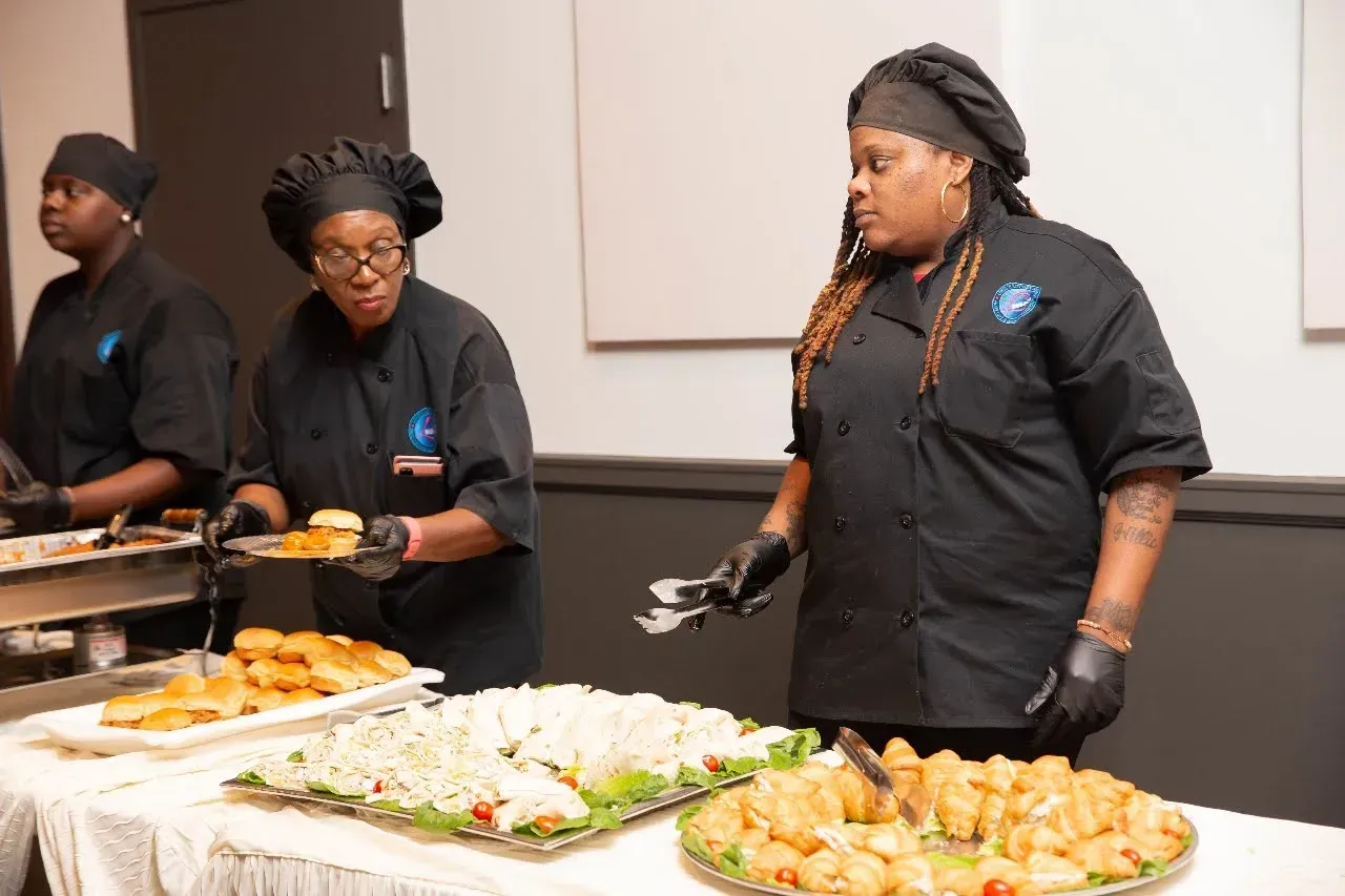 Three catering staff serving food buffet-style at a table in a meeting room