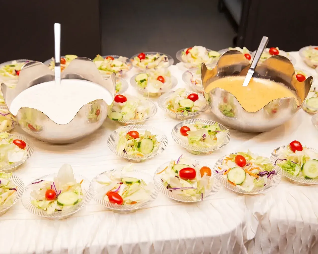 Dessert table with bowls of creamy pudding, fruit, and cherries, each with a spoon, on a white cloth tablecloth