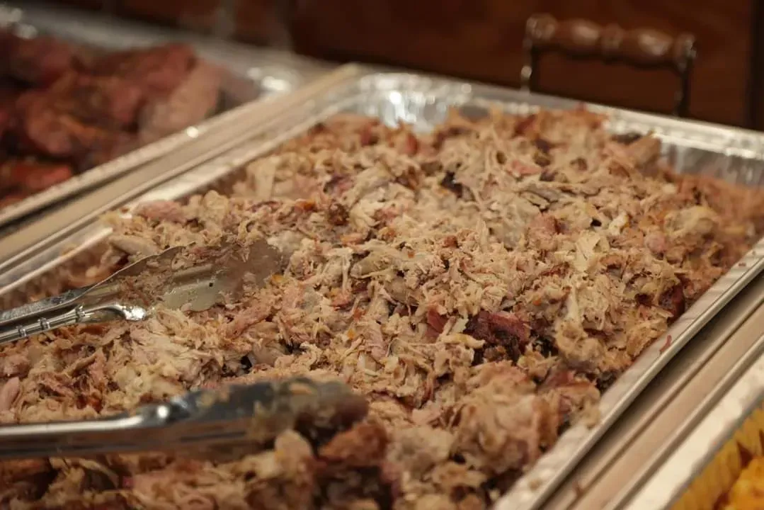 Tray of shredded meat at a buffet with serving tongs