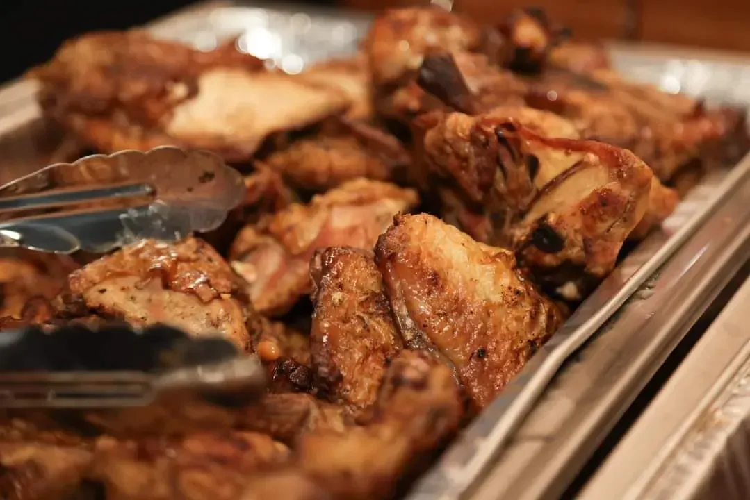 Tray of grilled chicken pieces with serving tongs at a buffet