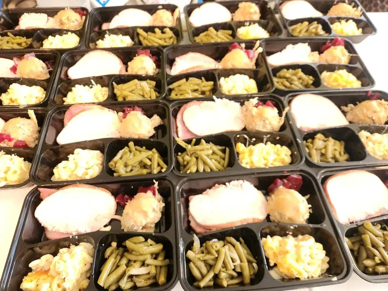 Rows of black meal trays with rice, vegetables, and noodles, arranged neatly for catering.