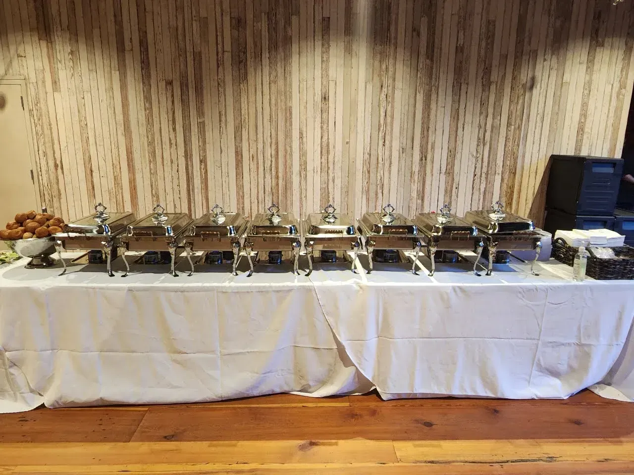 Buffet table with multiple stainless-steel chafing dishes and serving trays against a striped backdrop