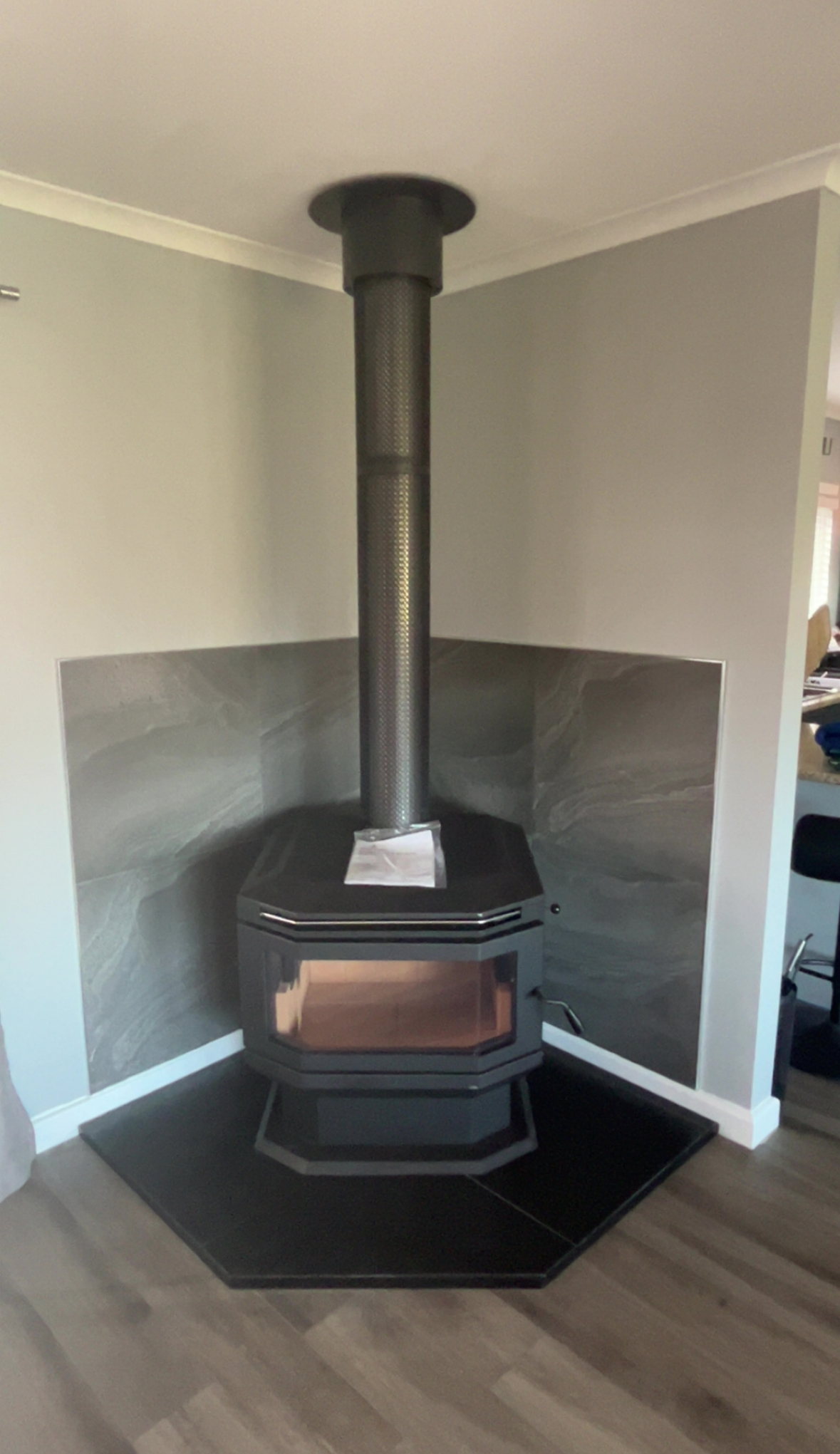Black Wood Stove With Tall Pipe in a Grey-walled Corner — The Flue Pro In Burnie, TAS