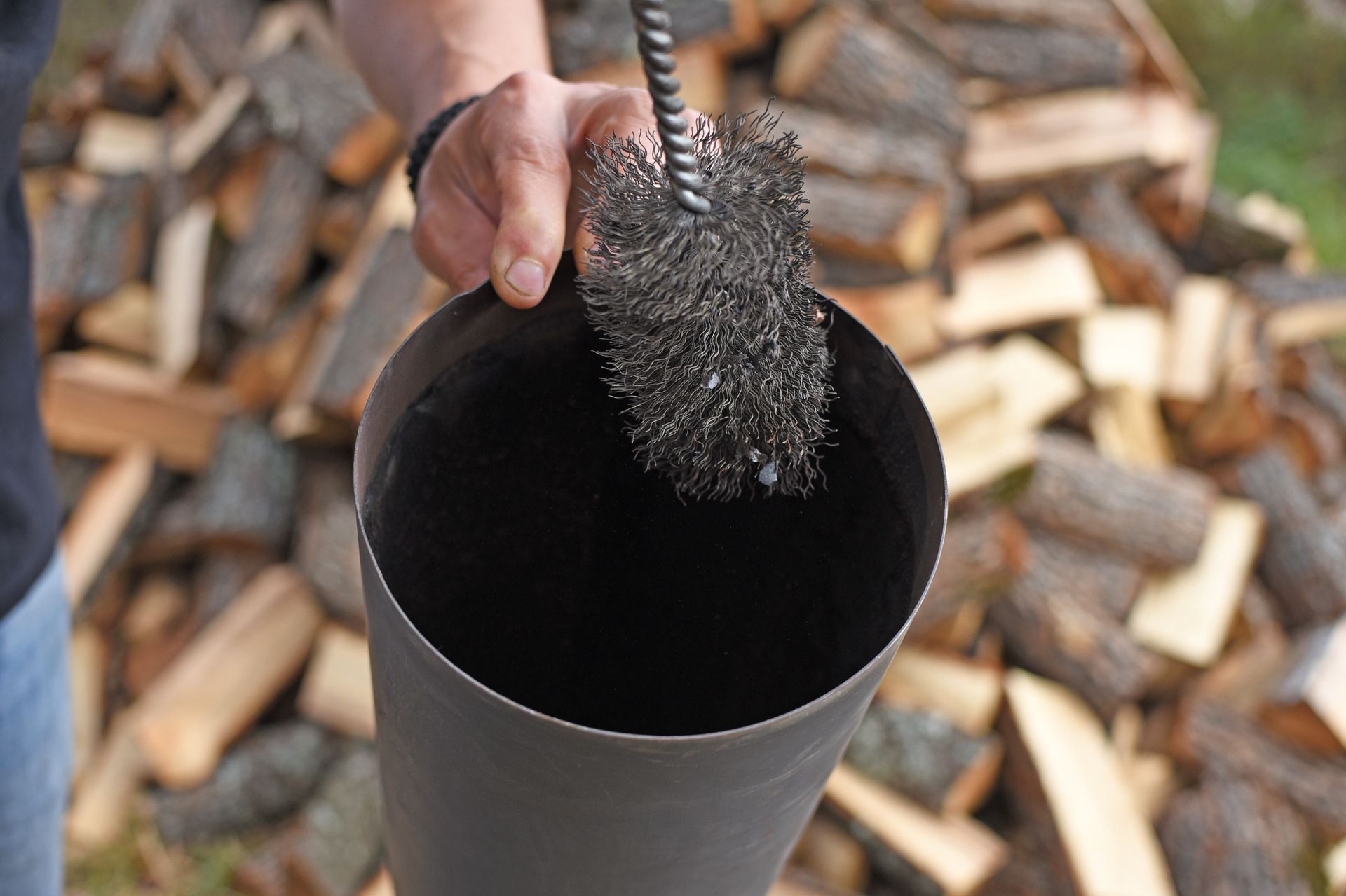 A Hand Holds a Wire Chimney Brush Over a Dark — The Flue Pro In Huntingfield, TAS