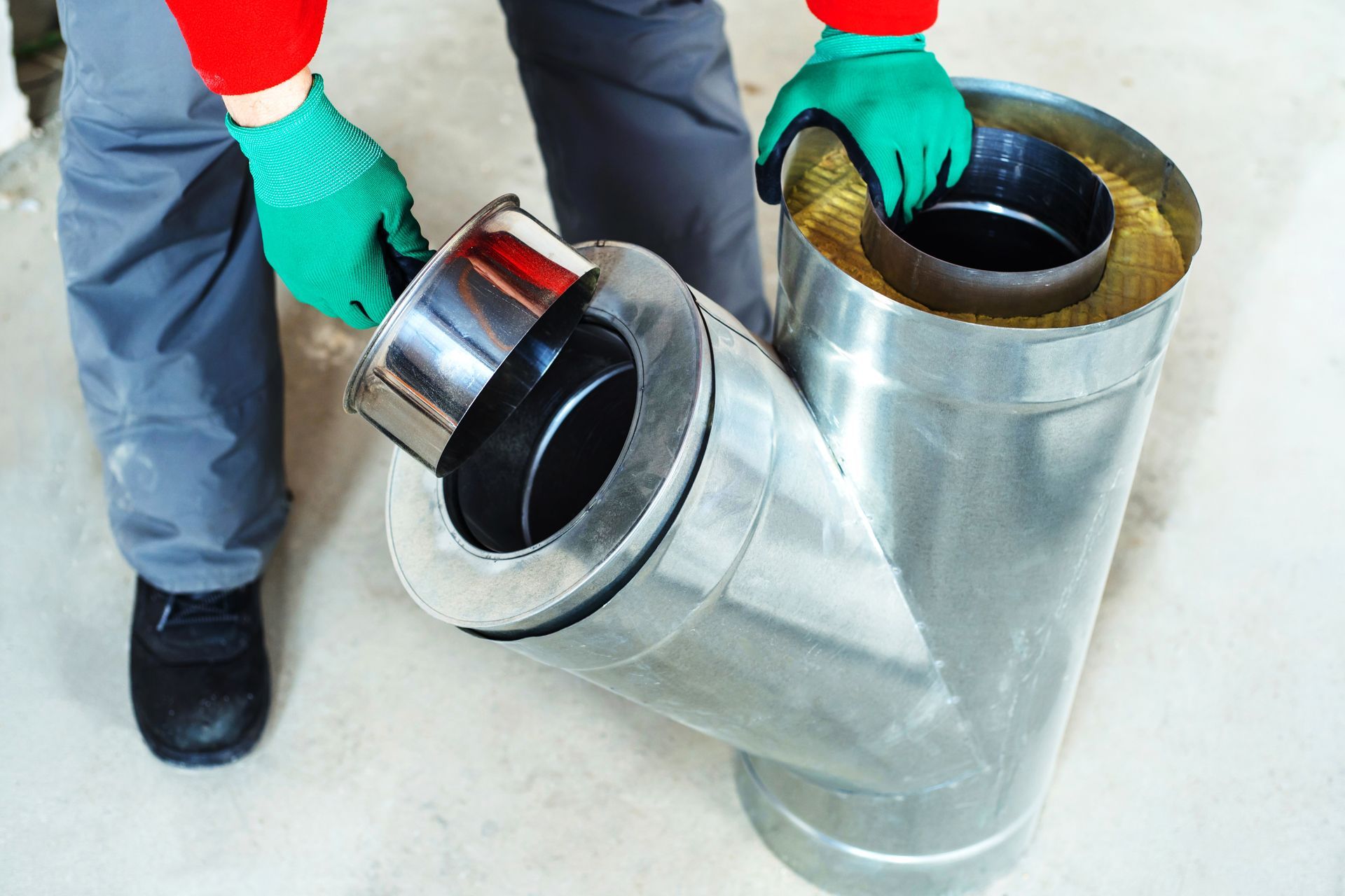 A Person Wearing Green Gloves Attaches a Metal Y-shaped Ventilation — The Flue Pro In Huntingfield, TAS