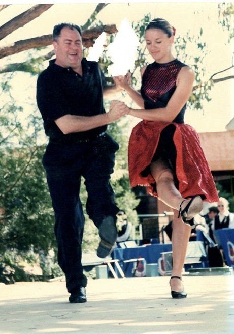 A man in a black shirt is dancing with a woman in a red dress