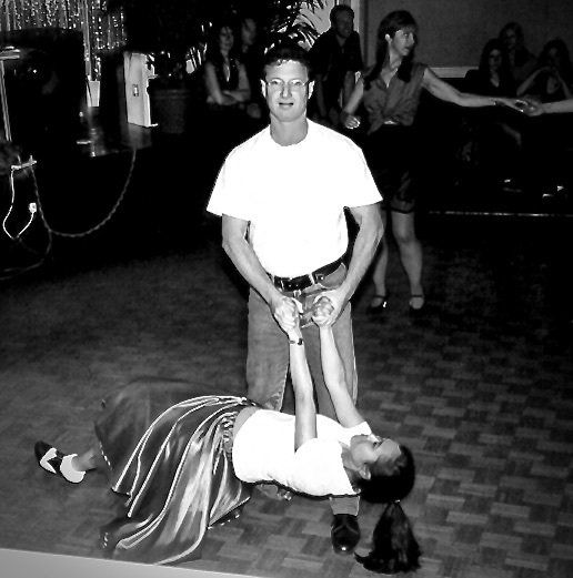 A person in a white shirt poses over a woman lying on the floor in a dimly lit room.