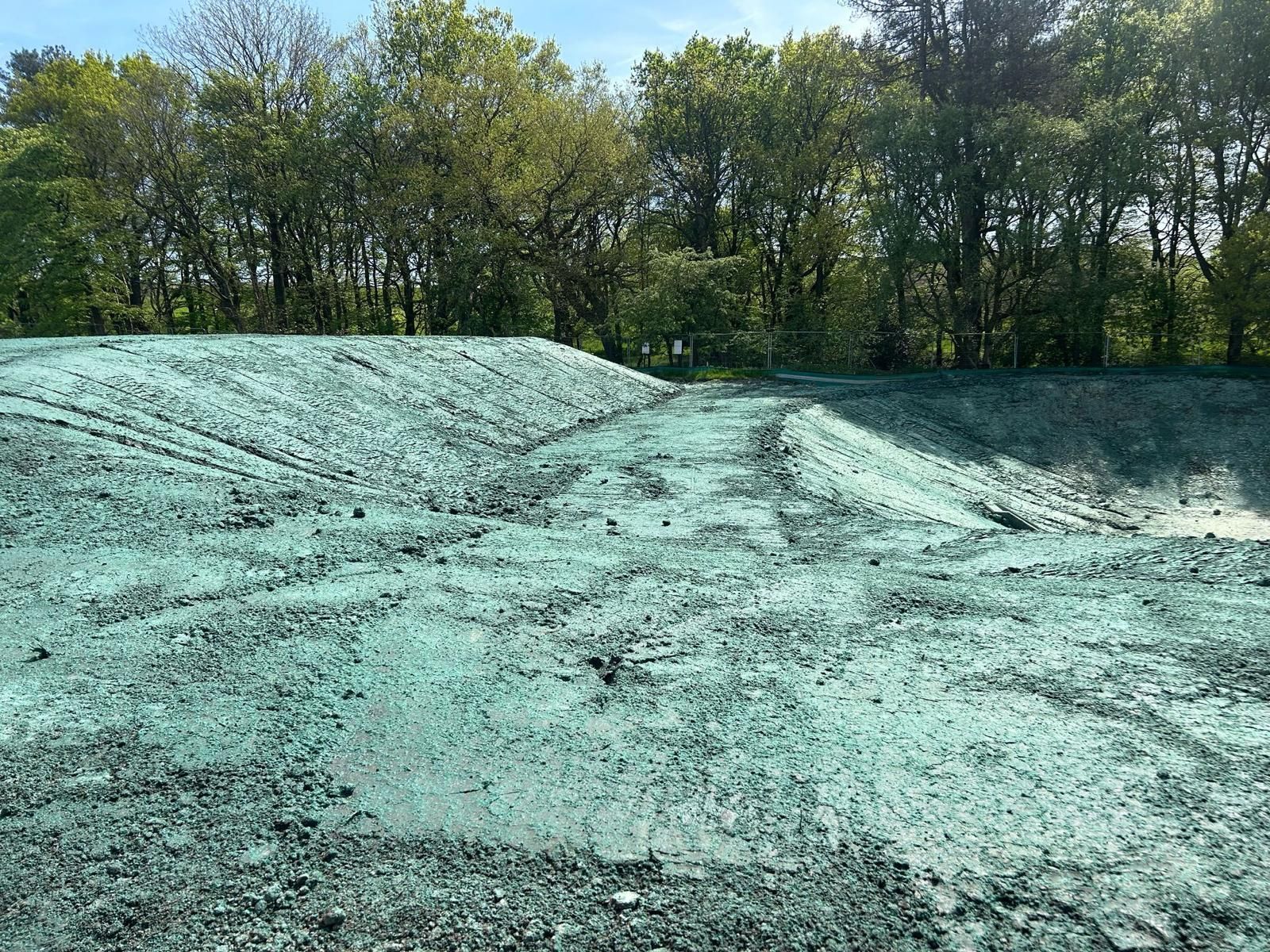 A freshly seeded hillside covered in green, with trees in the background under a blue sky.